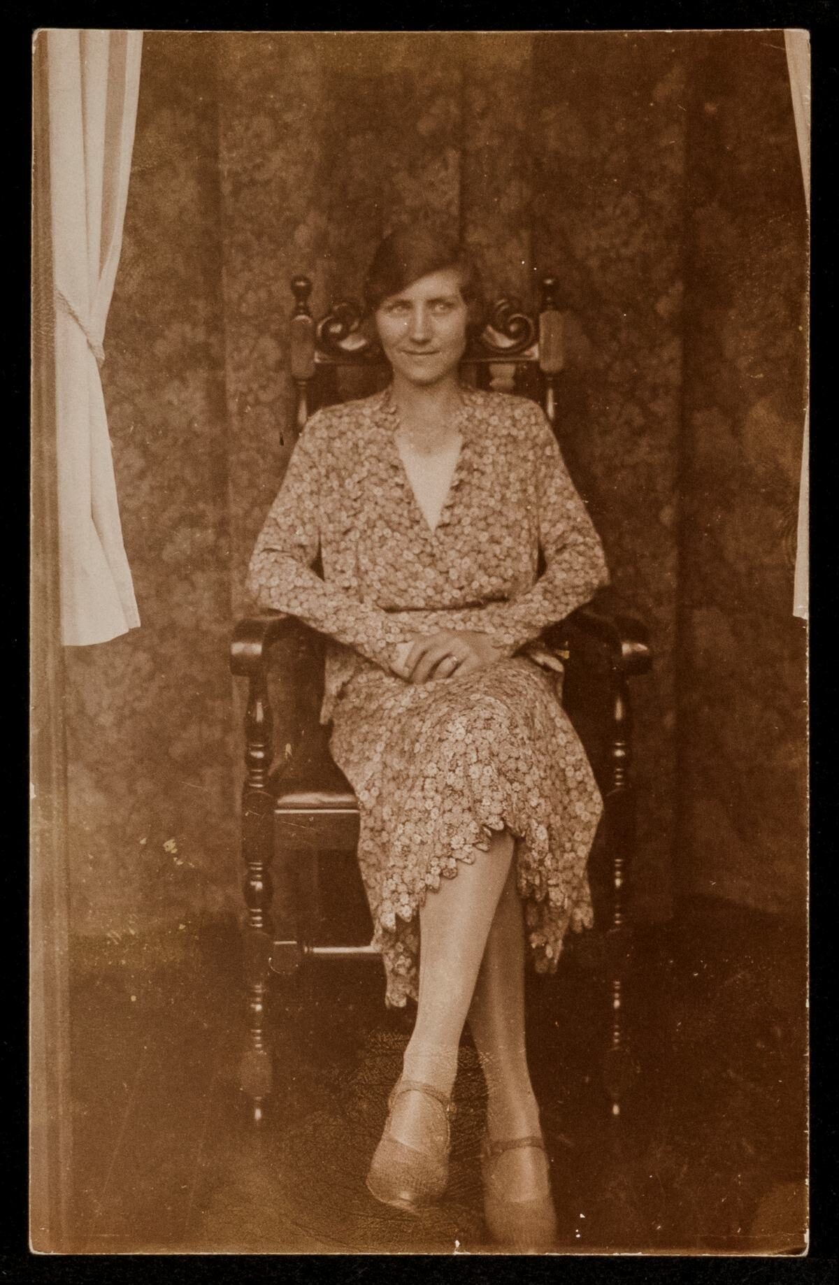 A woman in a vintage dress sitting in a chair, with a soft focus background