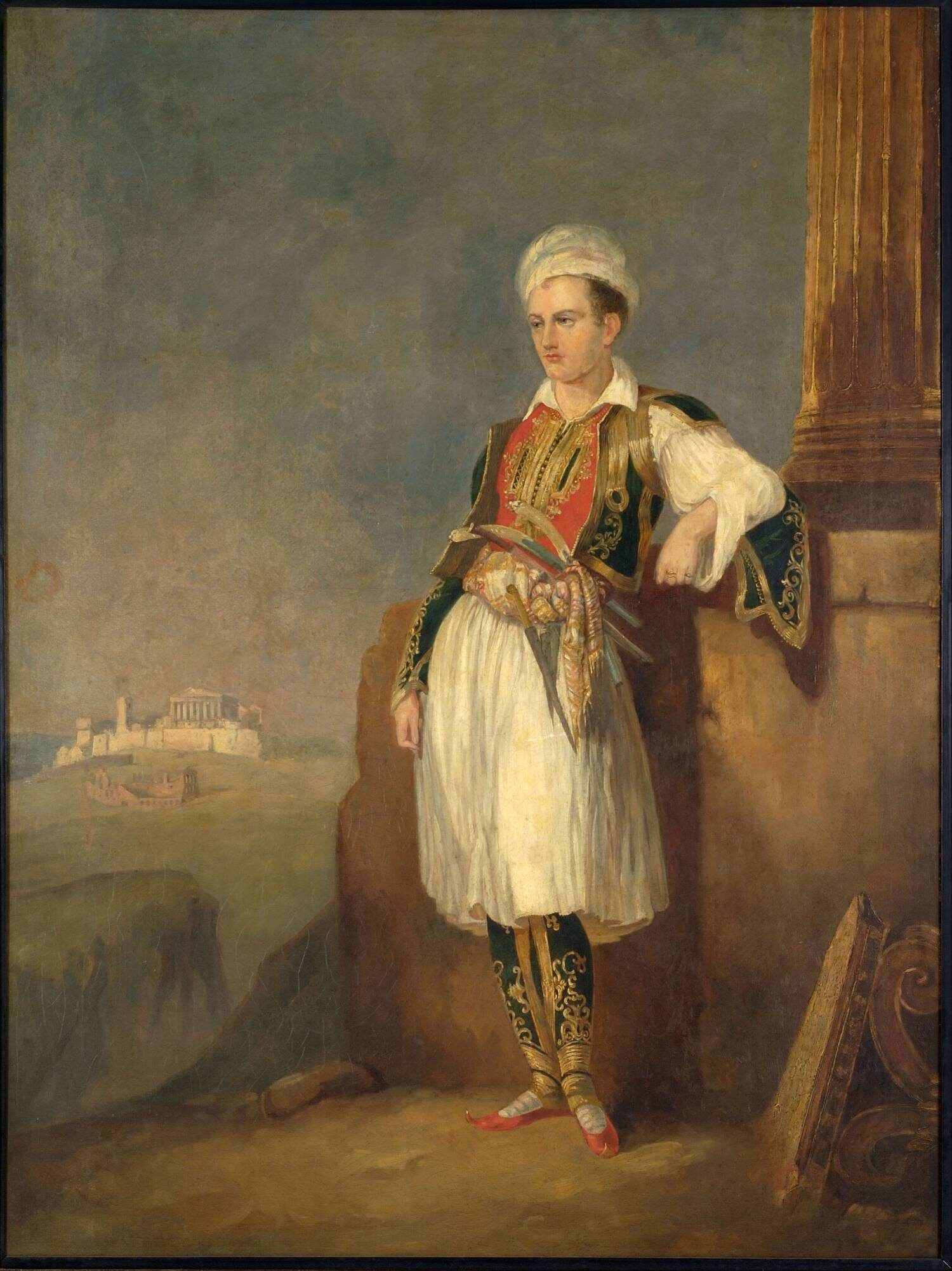 A young man in traditional Greek dress stands confidently, leaning against a stone. He wears a white skirt, colourful vest, and a hat