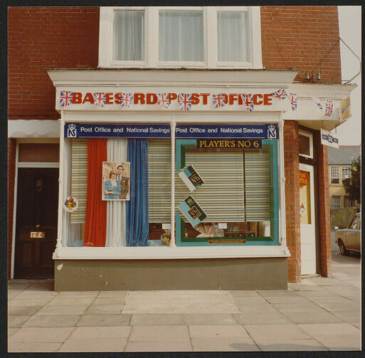 A post office storefront with a red and white sign, blue and white curtains, and closed shutters