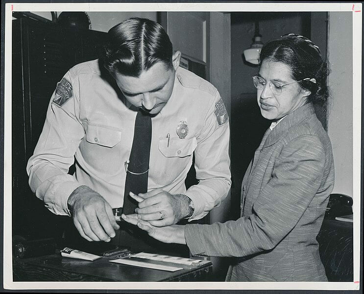 A police officer takes fingerprints from a woman in a small office