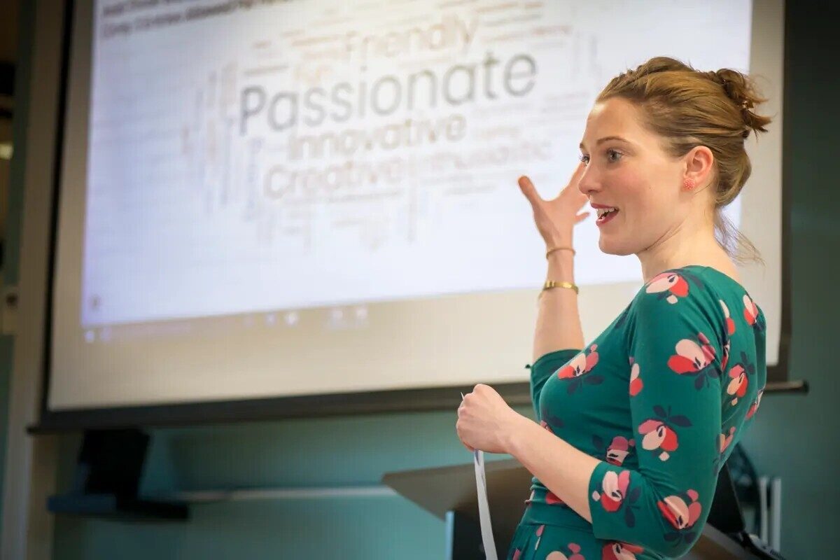 A woman in a green dress presenting against a digital screen showing a word cloud of motivational words