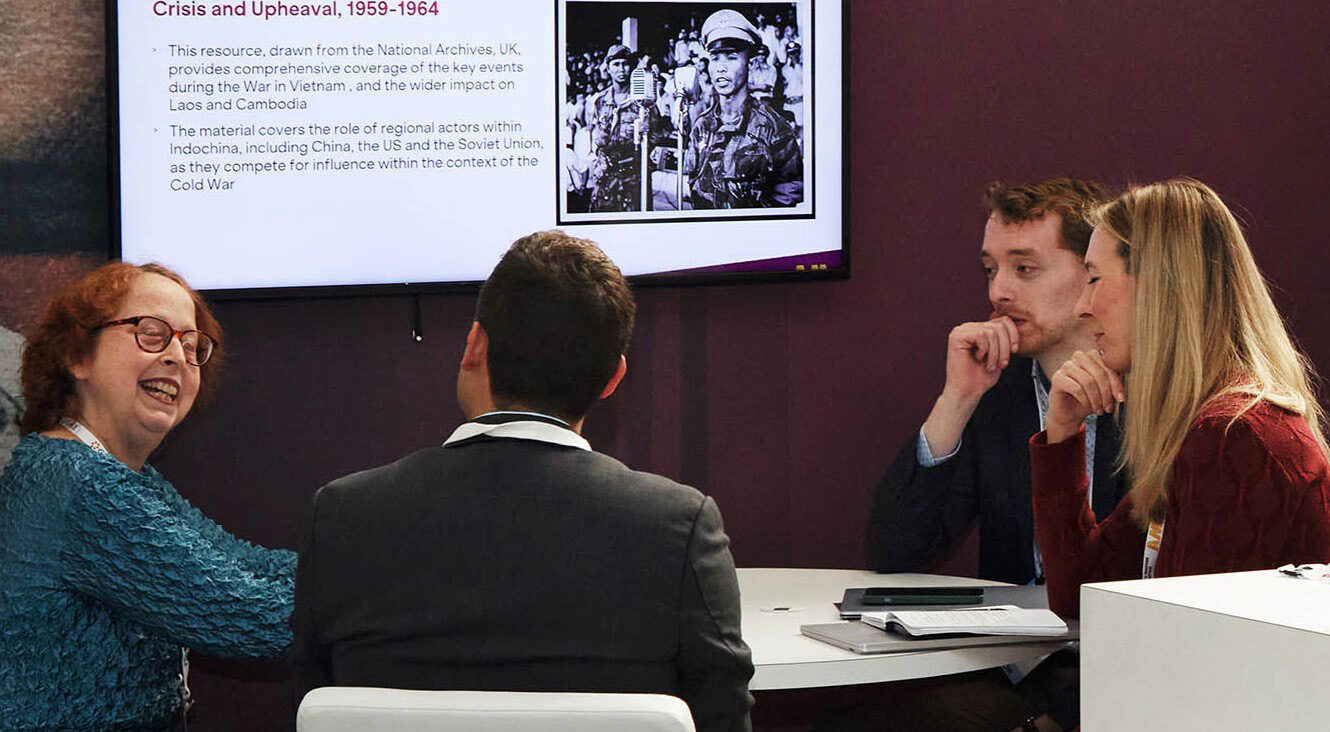 Four people sitting at a table engaging in discussion, with a screen showing notes about Vietnam, Laos, and Cambodia.