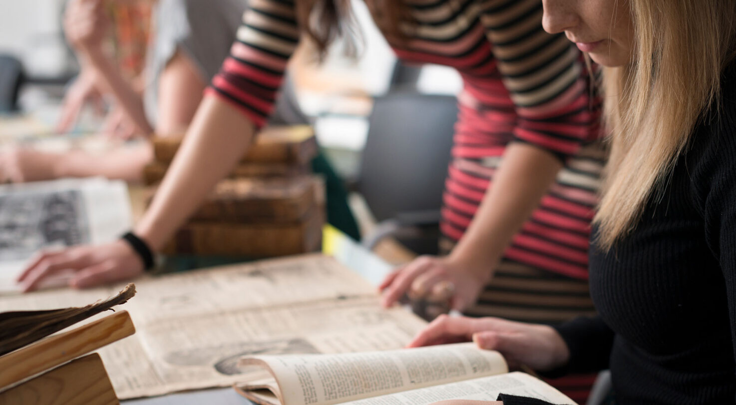 Two people examining old books on a table, with one reading a book.