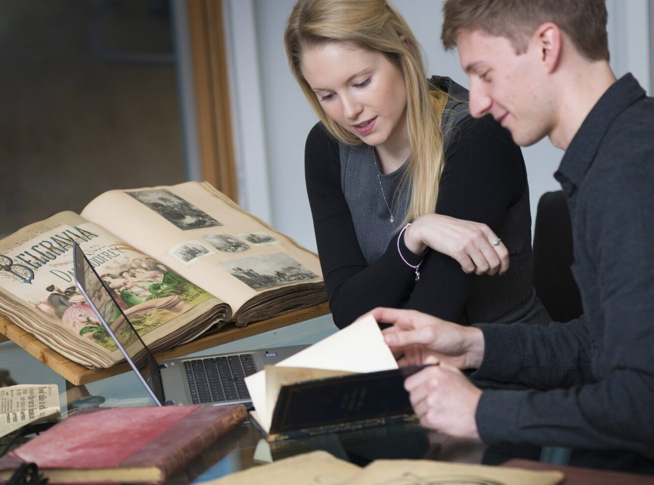 Two young people studying together at a table, with open books and a laptop.