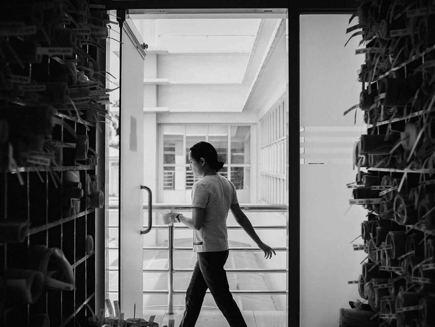 A person walking through a doorway, holding a cup, with organised rolls of archival papers on both sides.
