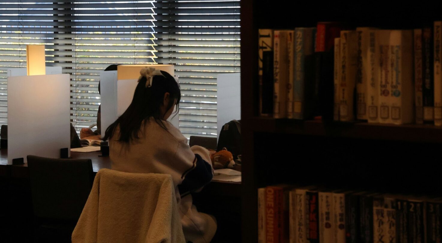 A person studying at a library table behind privacy screens, with sunlight through blinds.