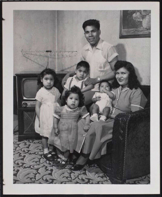 A family portrait with a man, woman, and four children in front of a vintage television.