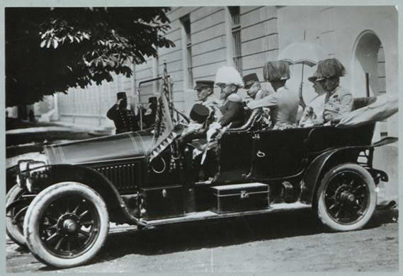 A vintage black car with four passengers, including a child, parked on a street.