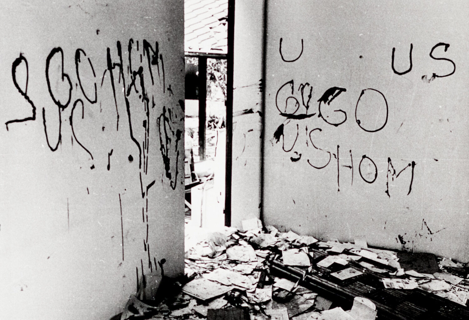 A dilapidated room with graffiti on the walls, debris on the floor, and a doorway visible