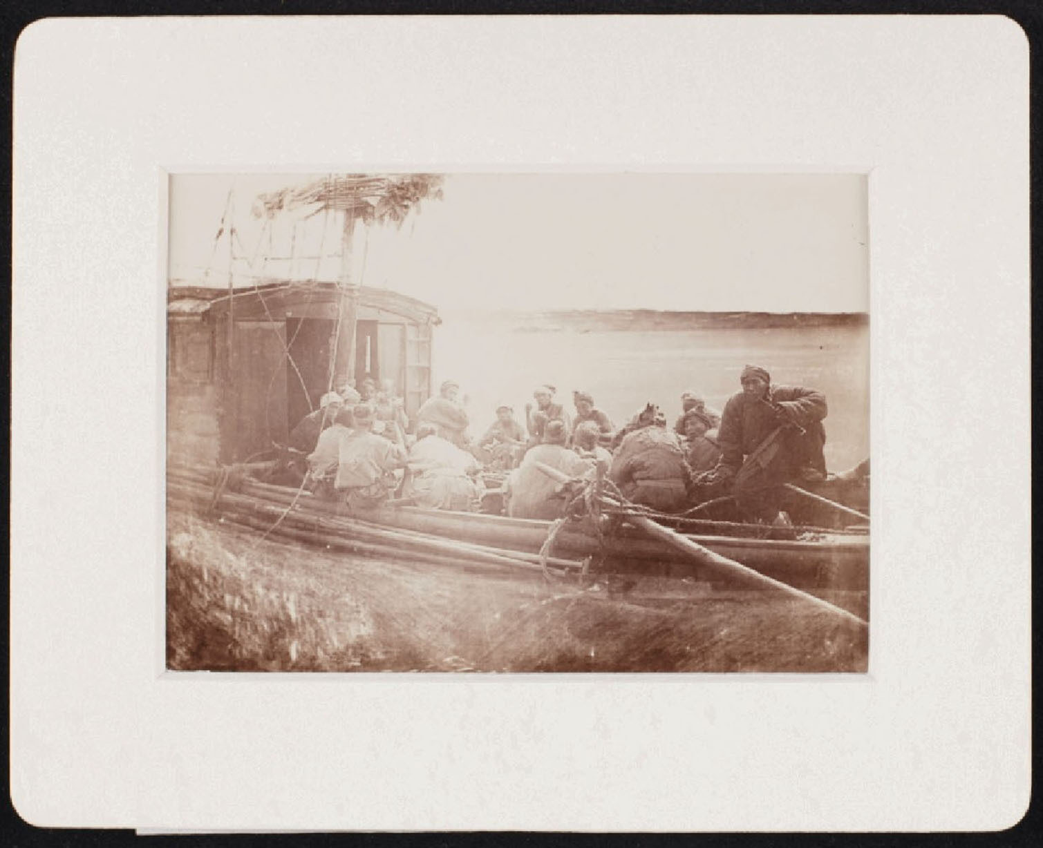 A group of people sitting in a boat near a river, with a cabin in the background