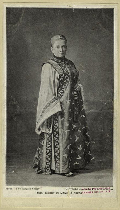 A person dressed in elaborate ceremonial robes, standing with one hand on their hip