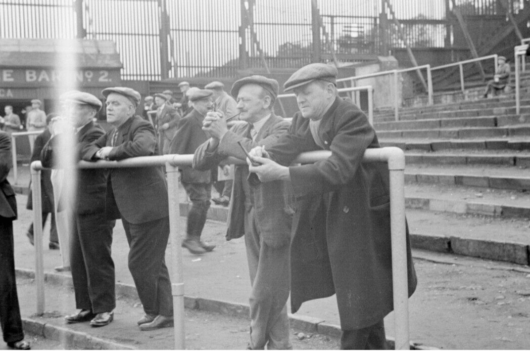 Football spectators gathered beside the terraces at a football ground during wartime.
