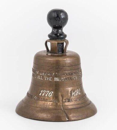 A bronze bell with an inscription, a black handle on top, and dated 1776 and 1892.