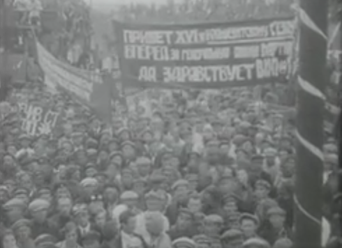 A large crowd gathered at a rally, holding banners with text. The atmosphere appears festive with decorations.