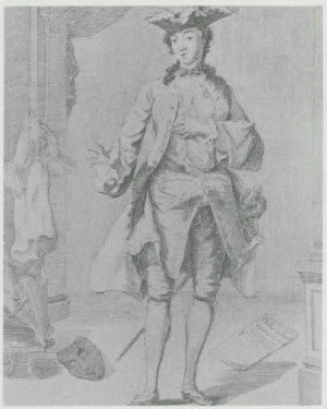 An actress dressed as a standing man in eighteenth-century clothing with a hat, gesturing with one hand. A mask and paper are on the floor.