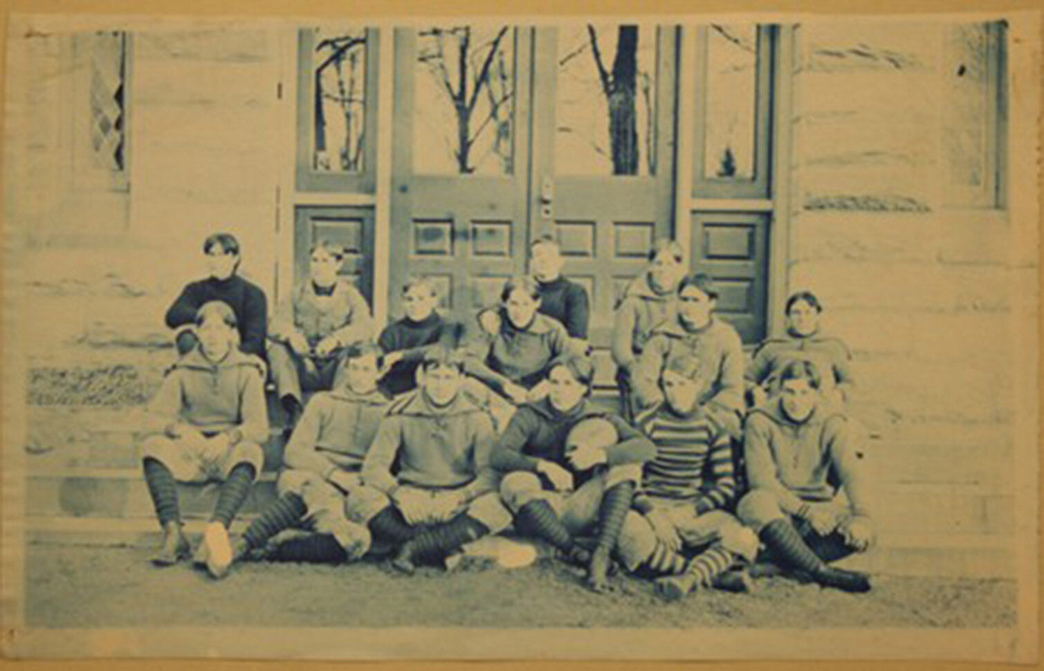 Historical football team posed on steps, wearing sweaters and striped socks.