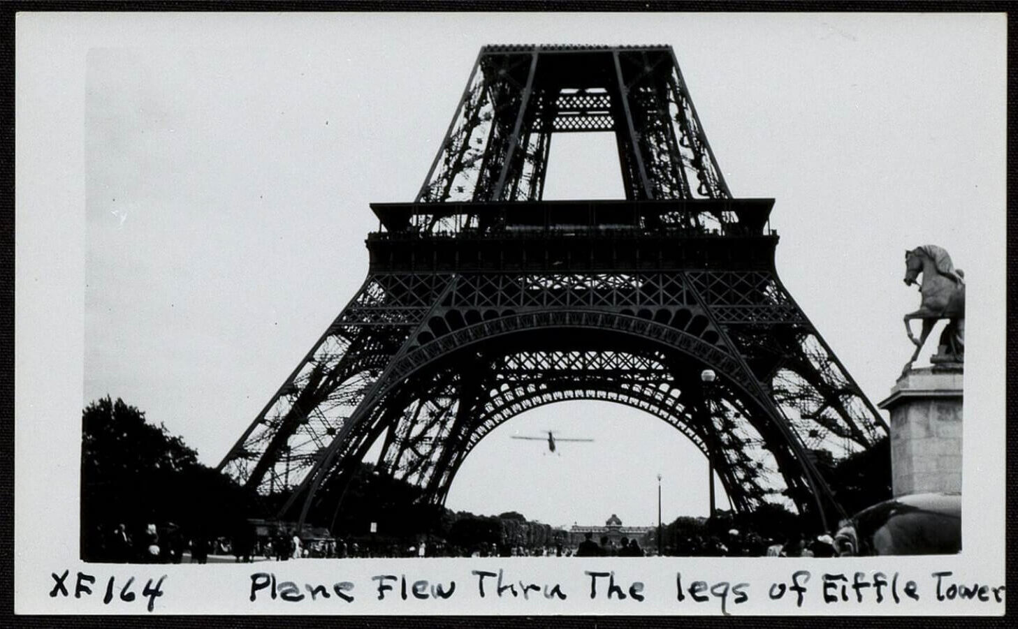 The Eiffel Tower with a plane flying under its legs, black and white photo