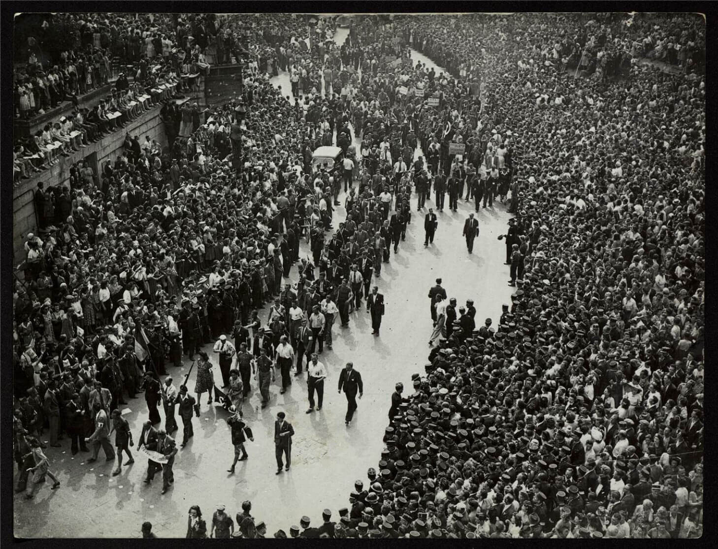 A large crowd watches a parade in a city street, filled with people and banners