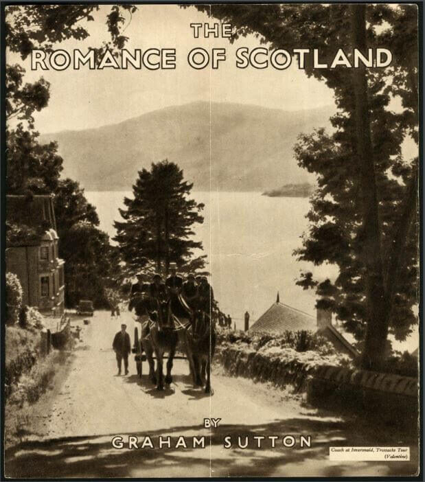 A scenic view of a lake surrounded by trees with two horses and people walking on a road.