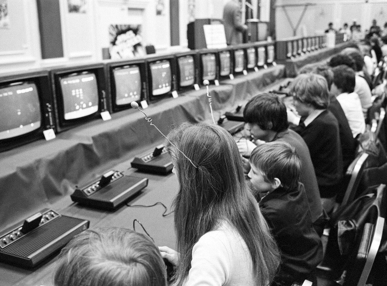 A group of children playing video games on old CRT monitors at a gaming event