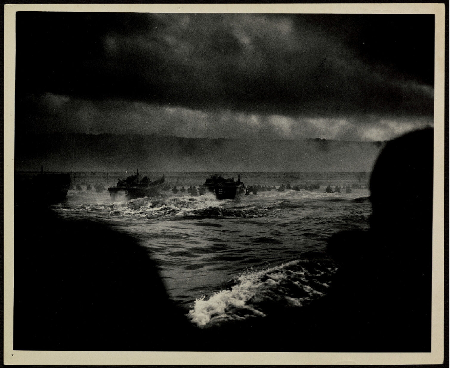 Dark silhouettes frame a stormy sea with crashing waves; boats cut through rough waters under dramatic clouds on D-Day