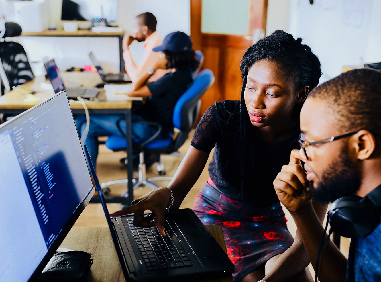 Two people focus on a laptop screen in an office, discussing coding work