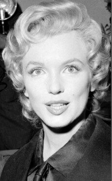 A classic black and white portrait of a woman with curly blonde hair and a bright smile.