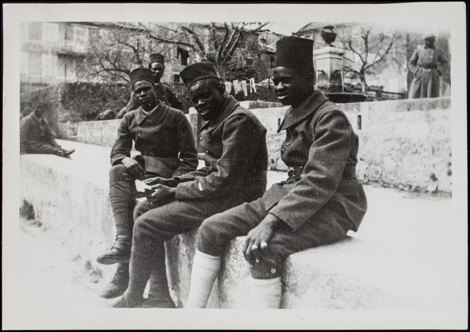 Three soldiers sitting on a bench, wearing uniforms and hats, in a historic setting
