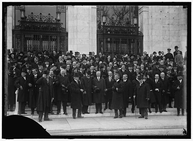 A large group of men in coats and hats, posing on steps outside a building.