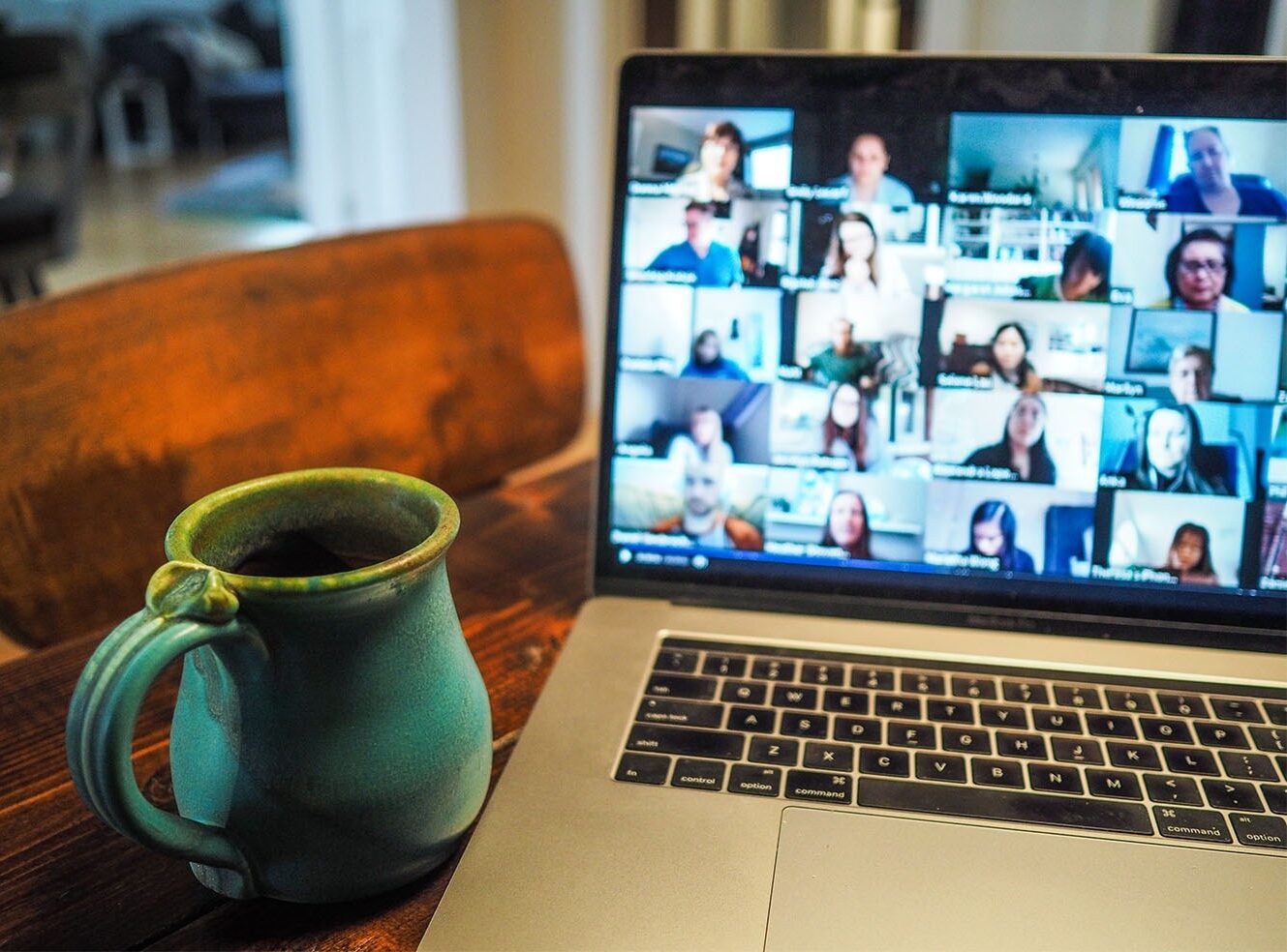 A teal mug filled with coffee next to a laptop showing a Zoom video call with many people.