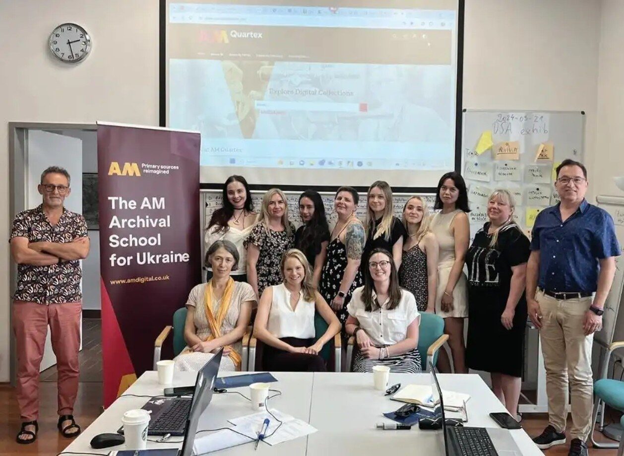 A group of professionals posed in front of a banner for the AM Archival School for Ukraine.