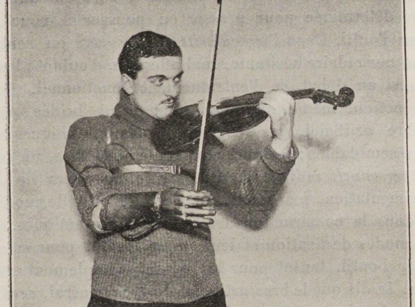 A man wearing a sweater and a prosthetic arm plays the violin. He has dark hair and a focused expression.