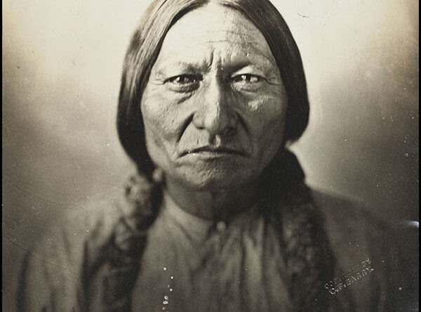An Indigenous North American person with long hair, wearing a light-coloured shirt, facing the camera head-on.