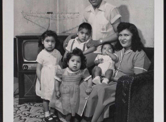 A family portrait with a man, woman, and four children in front of a vintage television.
