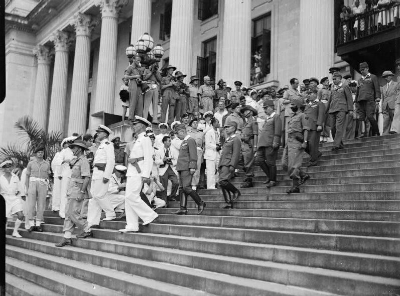 A large group of people, including military and officials, descending stone steps outside a grand building.