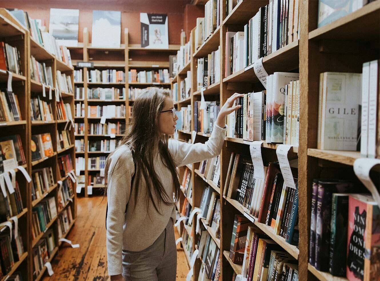 A person browsing books on a wooden shelf in a cosy library.