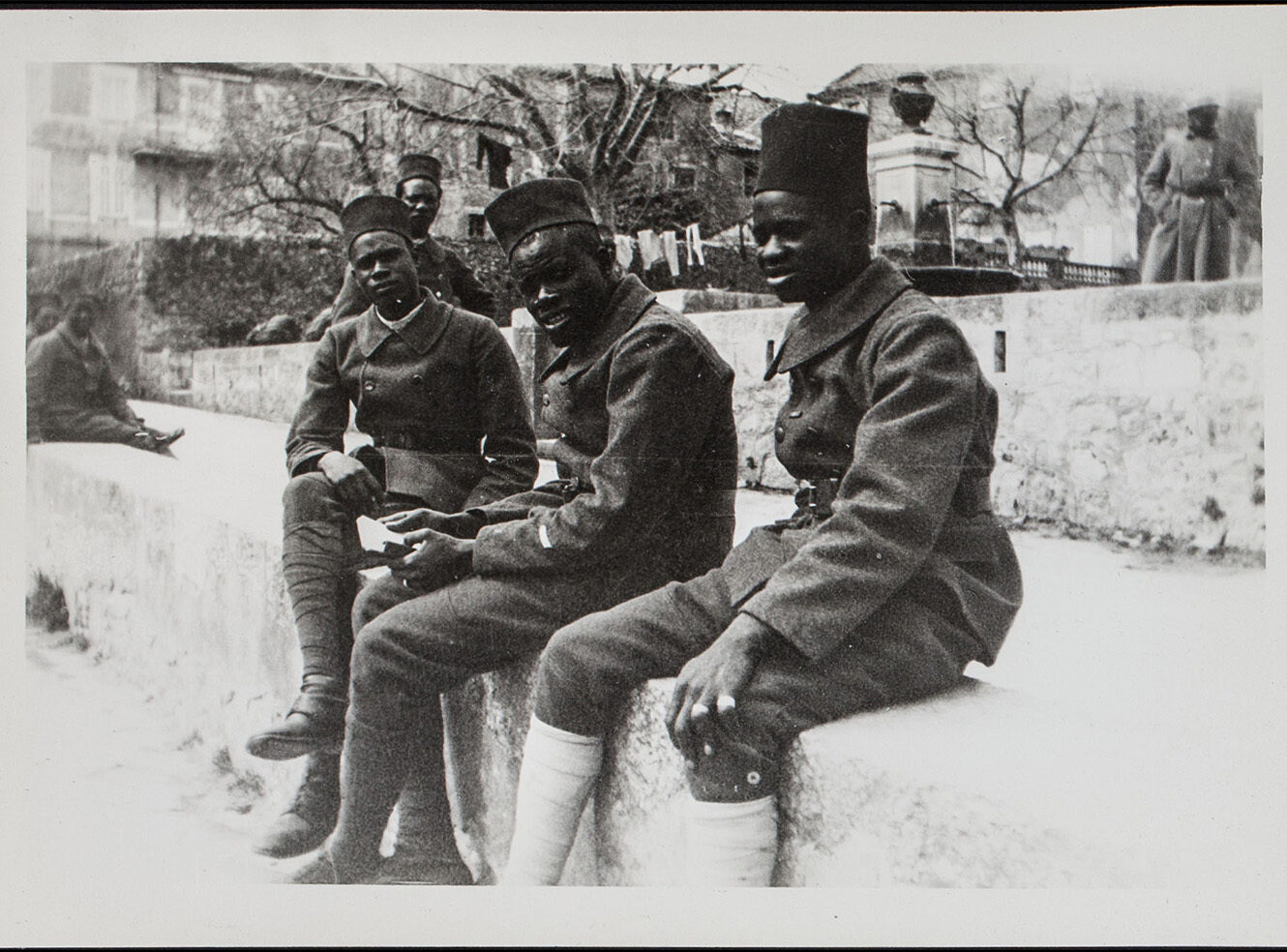 Three soldiers sitting on a bench, wearing uniforms and hats, in a historic setting