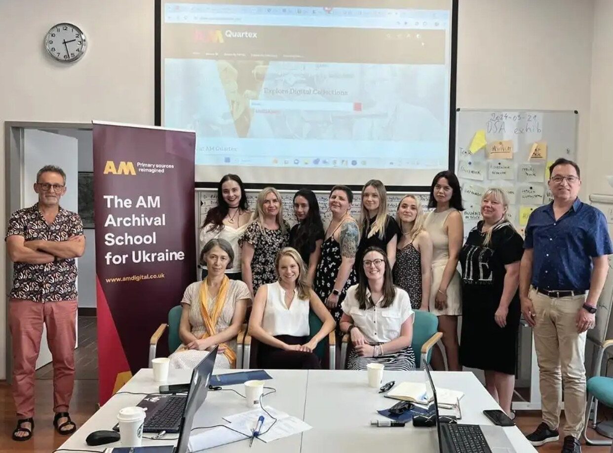 A group of professionals posed in front of a banner for the AM Archival School for Ukraine.