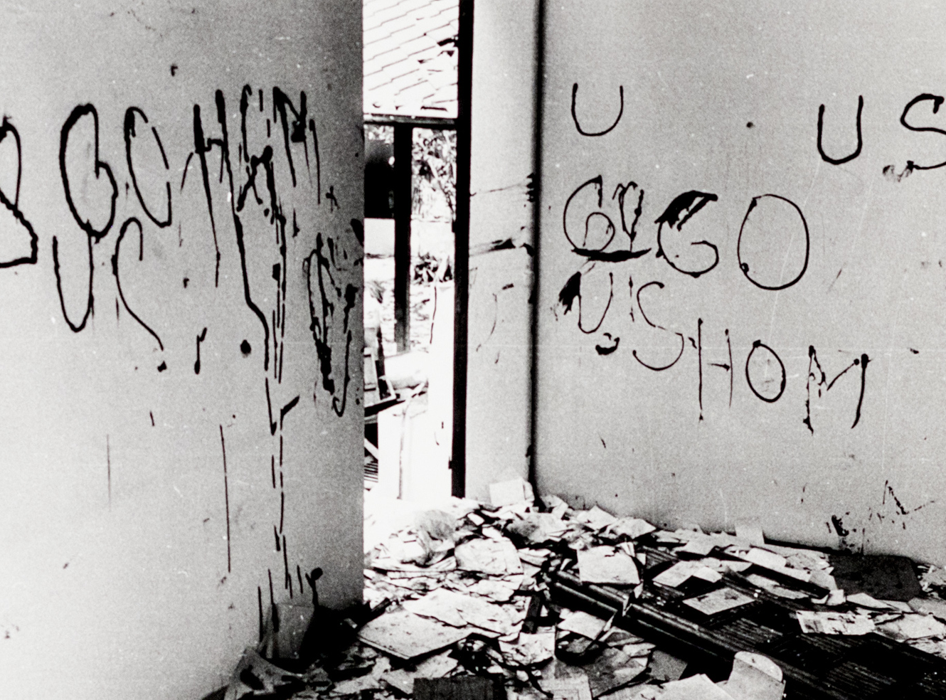 A dilapidated room with graffiti on the walls, debris on the floor, and a doorway visible