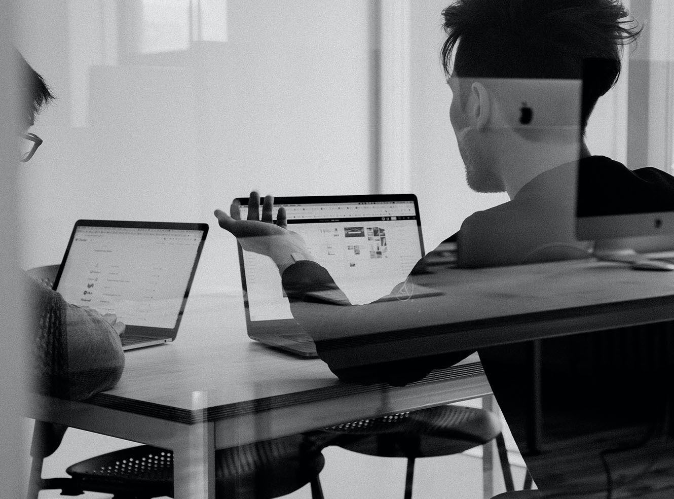Two people talking in a meeting room with laptops open.
