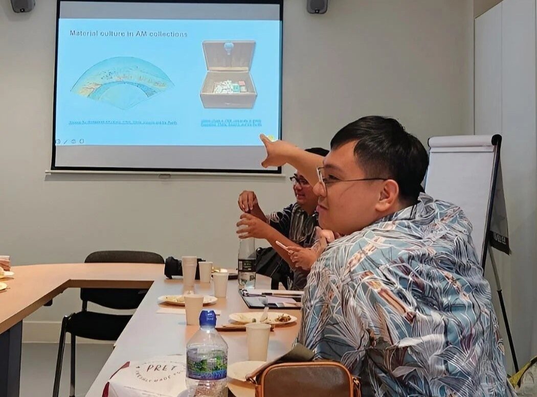 A group meeting in a room with a presentation on material culture, showing artifacts.