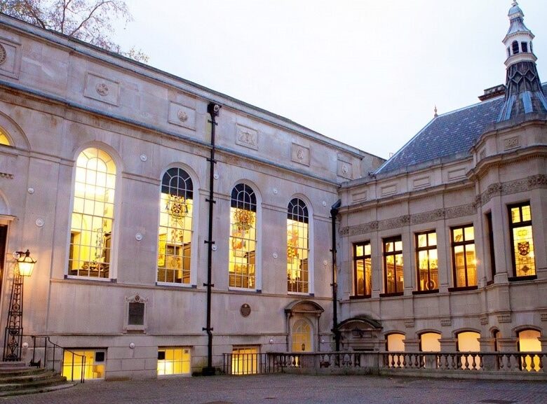 A blue door with wreaths leads to a historic building with large windows, glowing softly at dusk.