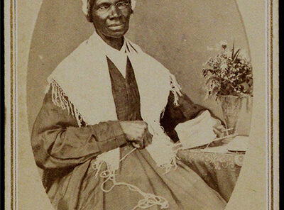 A historical figure, Sojourner Truth, seated with a decorative flower in a vase on her lap, dressed in a traditional outfit