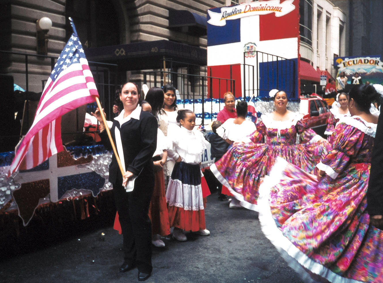 People celebrating with colourful dresses and a U.S. flag at a Dominican parade.