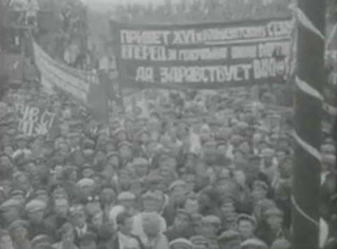 A large crowd gathered at a rally, holding banners with text. The atmosphere appears festive with decorations.
