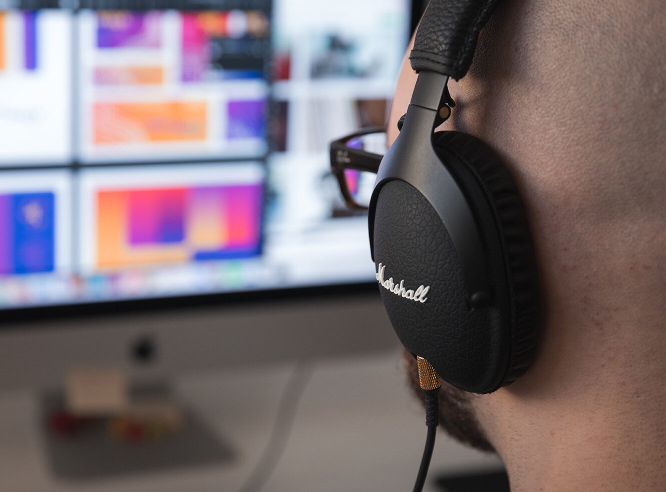 A person wearing Marshall headphones, focused on a colourful computer screen.