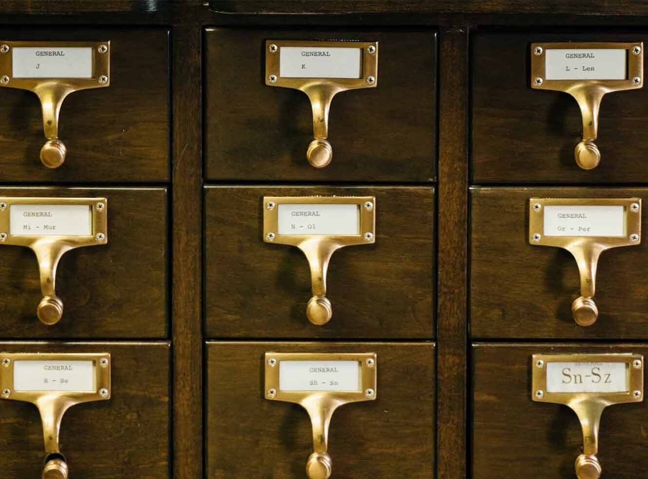 Wooden filing cabinet with brass handles, labeled drawers organized by letters.