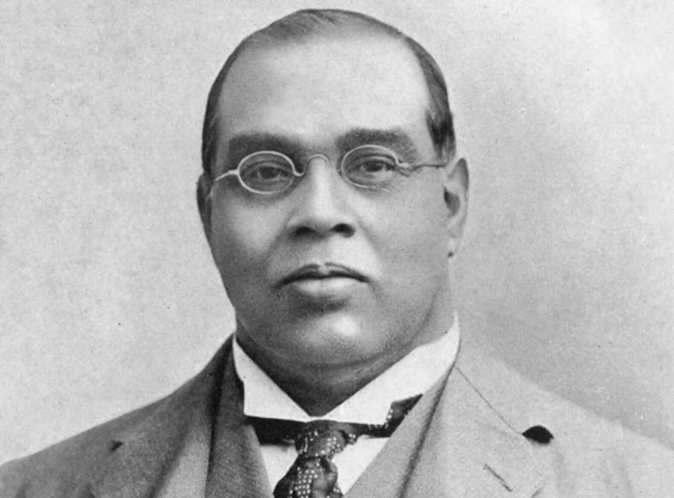 Portrait of a man in a suit and tie with glasses, smiling at the camera.