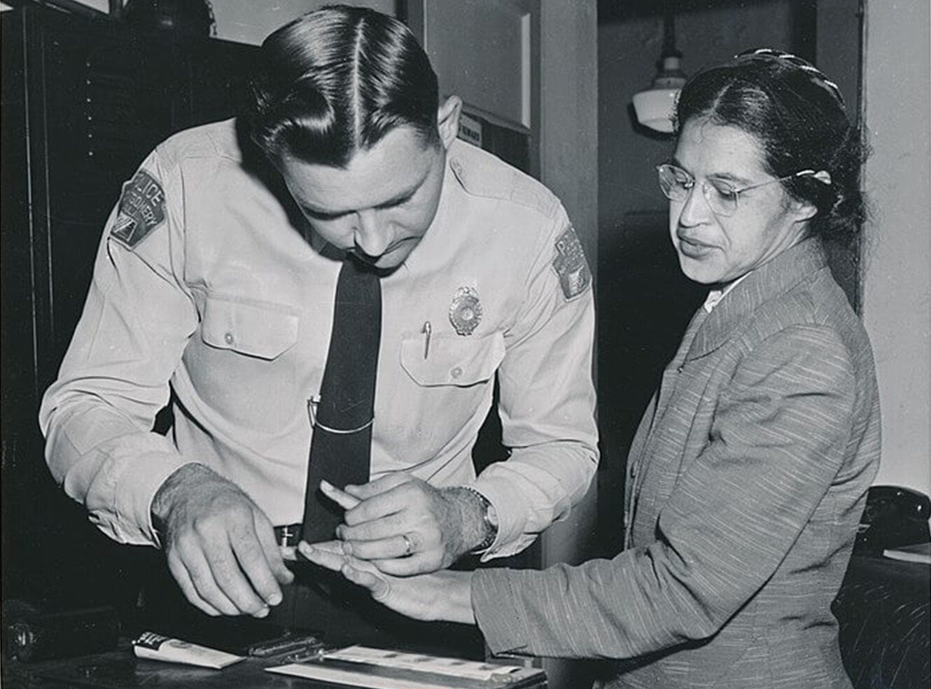 A police officer takes fingerprints from a woman in a small office
