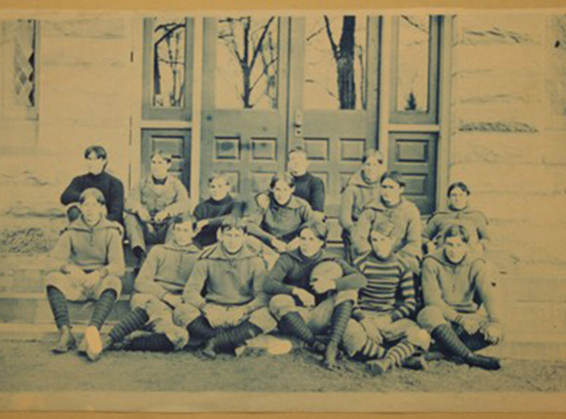 Historical football team posed on steps, wearing sweaters and striped socks.
